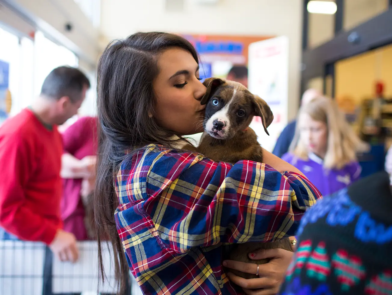 image of a woman in a plaid shirt kissing a puppy's face