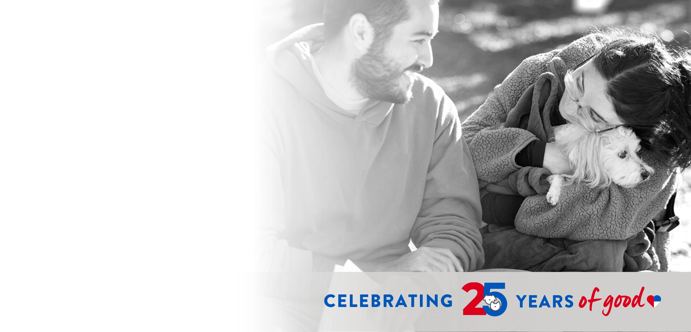 Man looks at a woman holding a small dog in her arms, text that reads "Celebrating 25 Years of Good"