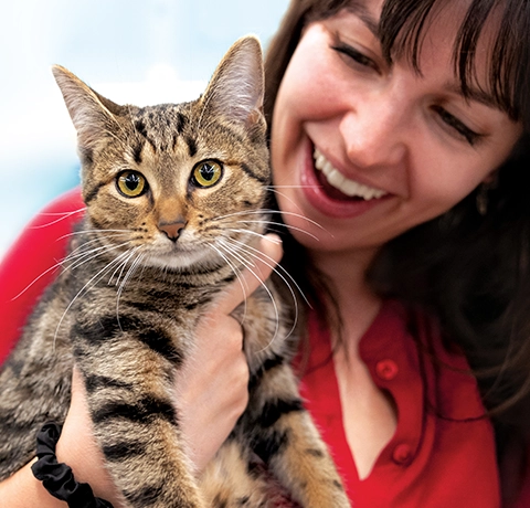 woman wearing red cardigan holds up a tabby cat