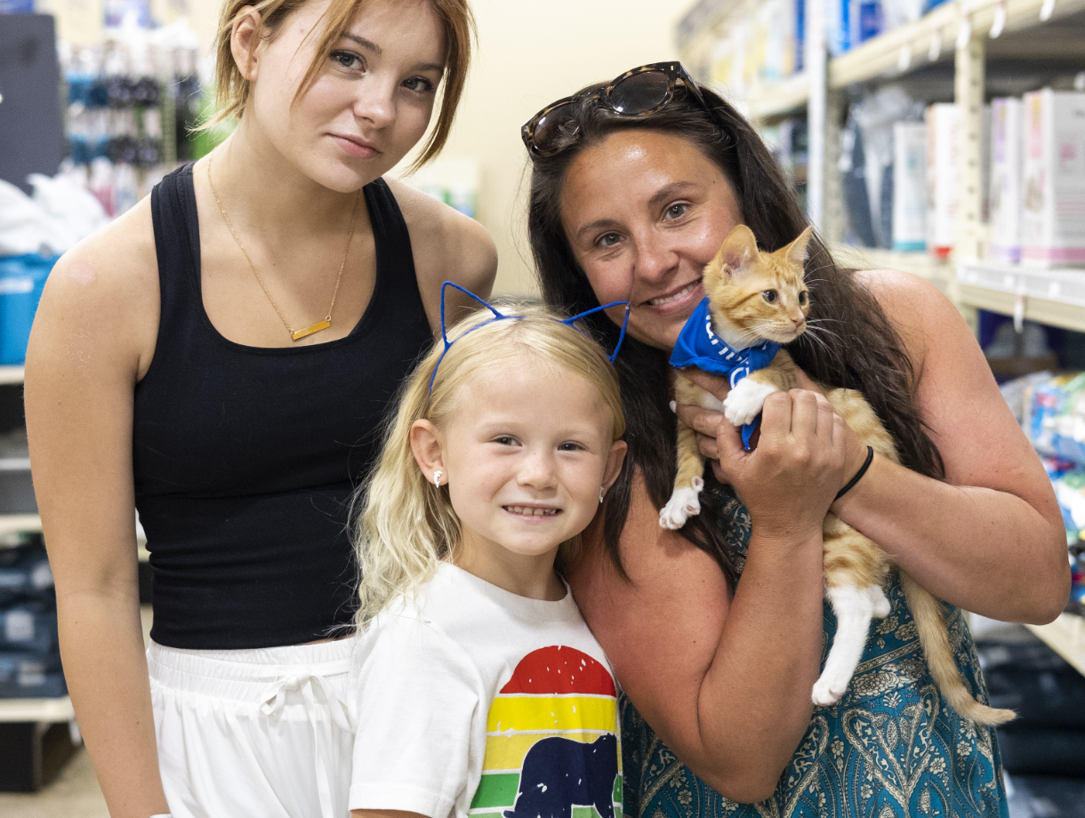 A family of three poses with their newly adopted orange kitten