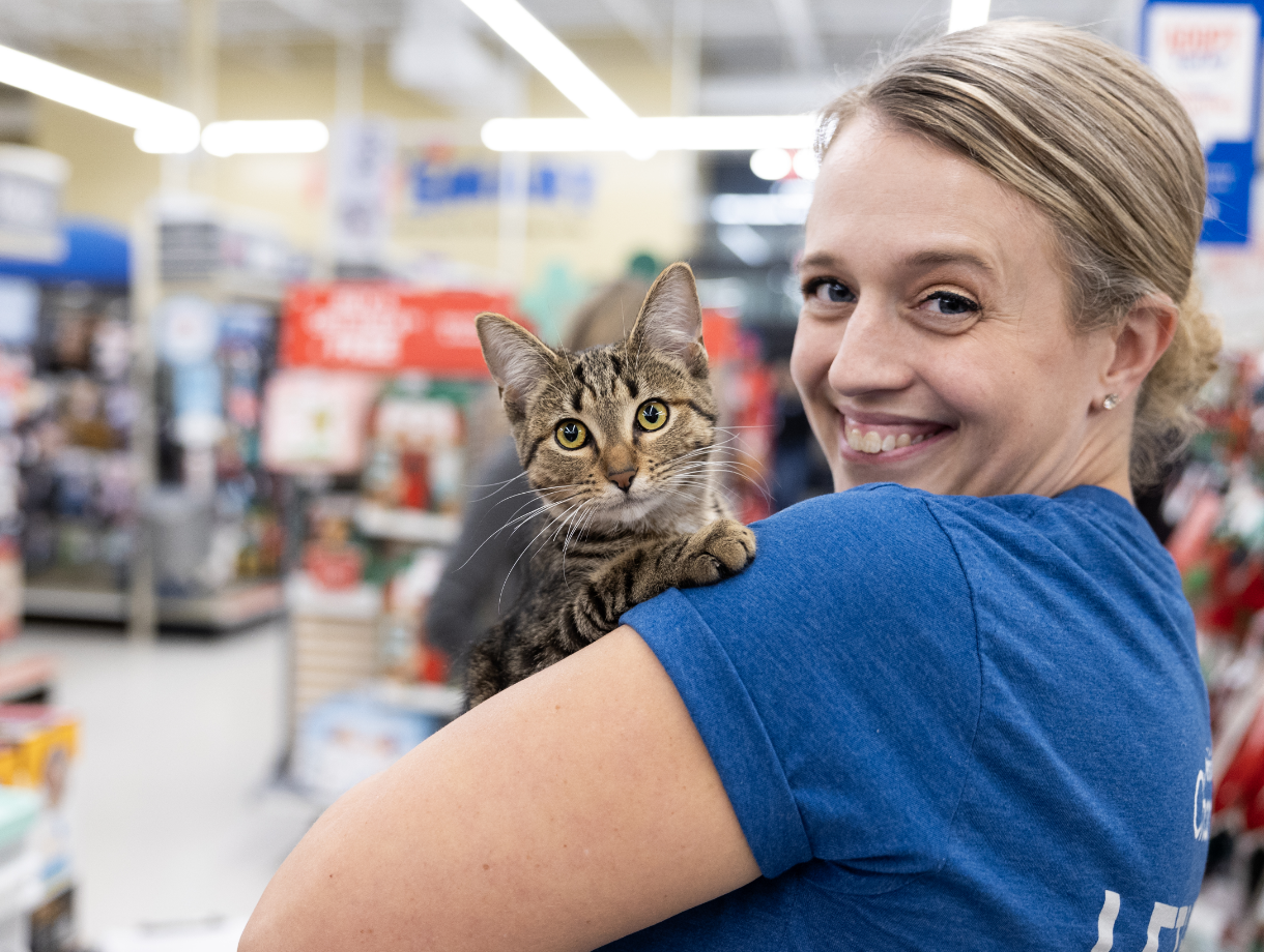 A smiling woman holds a cat in her arms in a PetSmart store